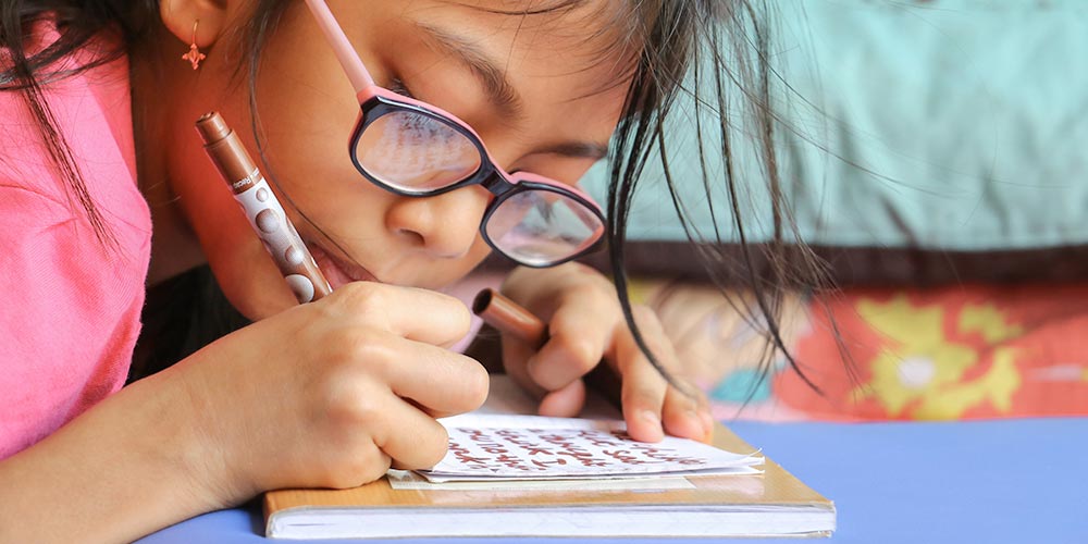 young girl with glasses writing a note with a marker